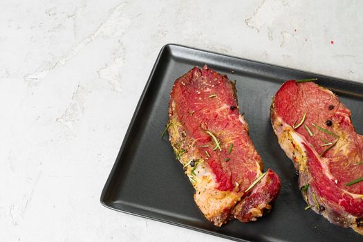 Two fresh raw meat steaks on black ceramic plate on stone background