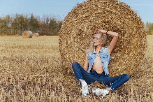 Beautiful girl villager posing in jeans near a bale of hay in a field