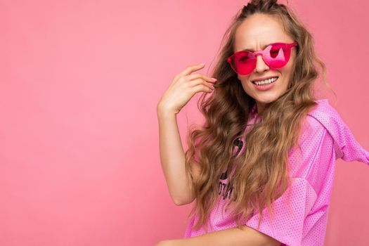 Closeup of attractive smiling happy young blonde woman wearing everyday stylish clothes and modern sunglasses isolated on colorful background wall looking at camera. empty space