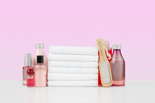 Stack of white towels and bottles of skincare on white table, front view