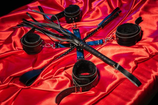 Top view of bdsm outfit. Bondage and whip crossed spank on the red linen. Adult sex games. Kinky lifestyle. - image