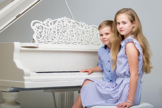Brother and sister, boy and girl studio portrait near the white piano.grand piano.Education, skills concept.