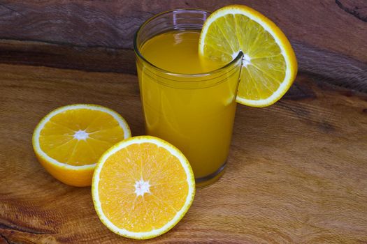 Glass of fresh orange juice with fruit slice and sliced valencia orange citrus fruit (Citrus x sinensis) on wood