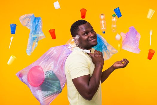 Problem of trash, plastic recycling, pollution and environmental concept - confused man carrying garbage bag on yellow background.