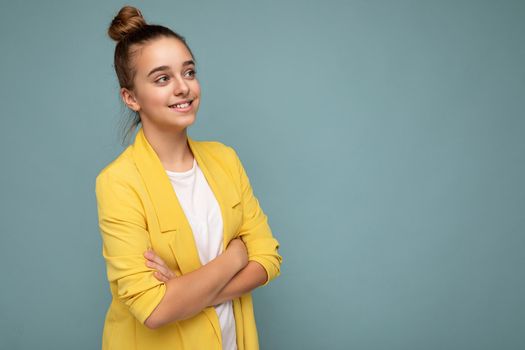 Side-profile photo shot of pretty positive happy smiling brunette little girl wearing trendy yellow jacket and white t-shirt standing isolated over blue background wall looking to the side. Copy space