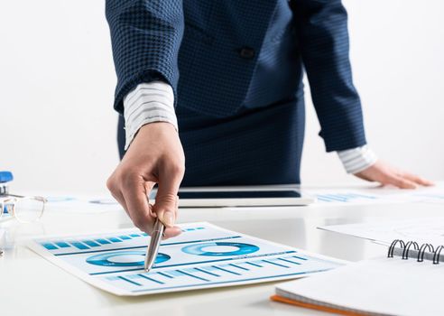 Businesswoman standing near office desk and analyzing financial charts. Successful corporate manager in business suit. Close-up woman hand with pen. Business presentation in conference room