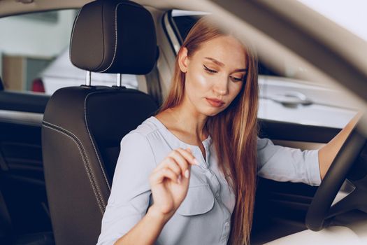 Attractive young woman sitting in new car in showroom close up