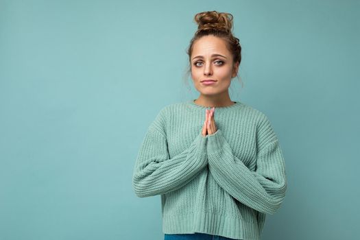 Photo of young positive beautiful blonde woman with sincere emotions wearing casual blue pullover isolated over blue background with copy space and doing namaste gesture. Yoga concept.