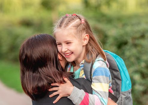 School girl hugging mother after classes in sunny park