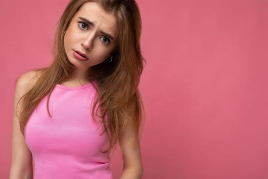 Sad young attractive dark blonde woman with sincere emotions isolated over background wall with copy space wearing trendy pink top. Negative concept.