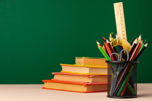 School supplies on wooden desk against green chalkboard front view