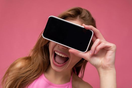 closeup Photo of overjoyed beautiful smiling young woman good looking wearing casual stylish outfit standing isolated on background with copy space holding smartphone showing phone in hand with empty screen display for mockup.