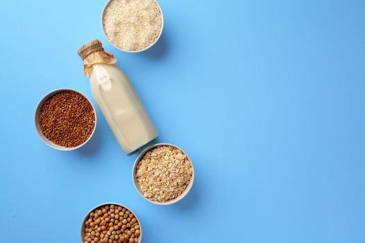 Vegetable milk concept with milk bottle and bowls with grains and nuts on blue background top view