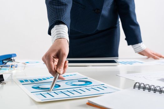 Businesswoman standing near office desk and analyzing financial charts. Successful corporate manager in business suit. Close-up woman hand with pen. Business presentation in conference room