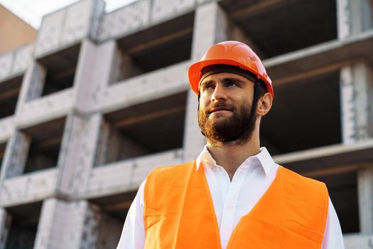 Builder wearing hardhat and safety vest standing on a commercial construction site, close up portrait