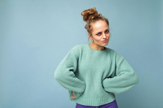 Shot of young sad upset dissatisfied angry pretty blonde woman wearing blue jersey isolated on blue background with empty space.