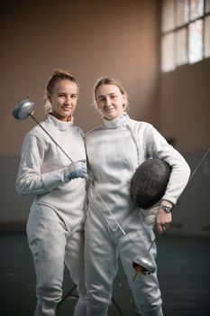 A portrait of two young women fencers holding swords