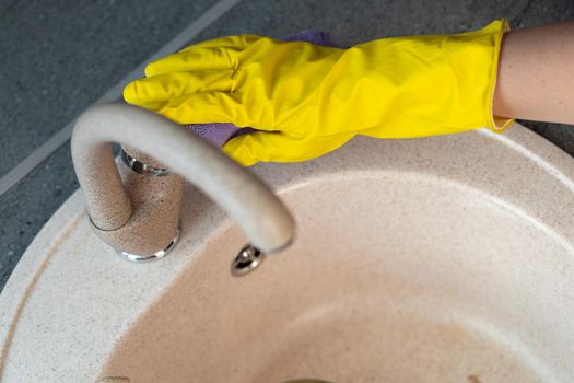 Hands in yellow gloves cleaning a sink with a sponge close up