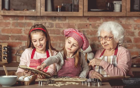 Grandma and granddaughters are spreading dough using a rolling pin