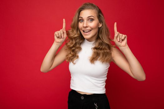 Photo of attractive positive surprised young woman pointing fingers up at copyspace presenting ads promo with wow omg sincere emotions wearing good look outfit isolated over background with free space.