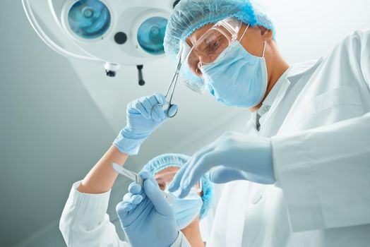 Woman nurse rubs forehead of man surgeon on operation on background of surgical lamp