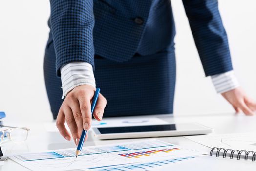 Businesswoman standing near office desk and analyzing financial charts. Successful corporate manager in business suit. Close-up woman hand with pen. Business presentation in conference room