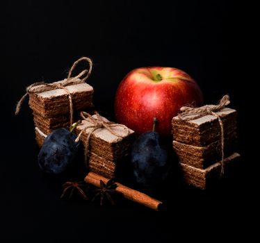 Apple pastila and cinnamon and star anise isolated on black background. Healthy snack concept. Slices of pastila tied with a twine, plums and red apple