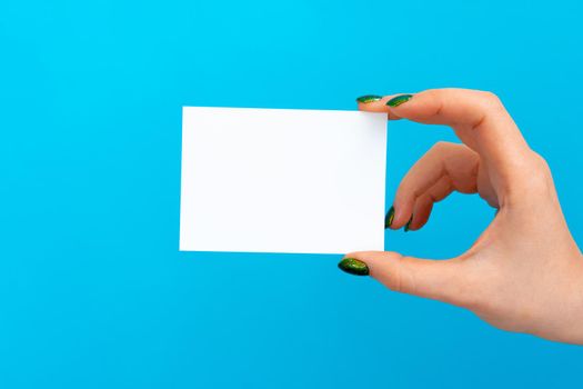 Woman hand holding blank card on blue background, close up.