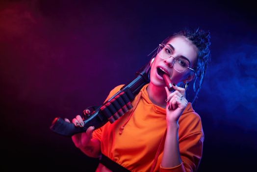 a sexy brunette in an orange jumpsuit with a shotgun on a dark background in neon light