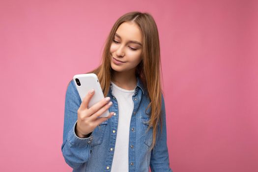 Beautiful young woman wearing casual clothes standing isolated over background surfing on the internet via phone looking at mobile screen.