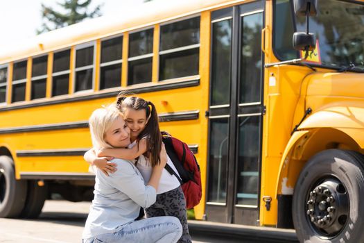 Mother escorts the schoolgirl with ponytails and a backpack to school.