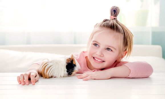 Portrait of happy smiling little girl hugging fluffy tricolor guinea pig. Adorable little child with pet