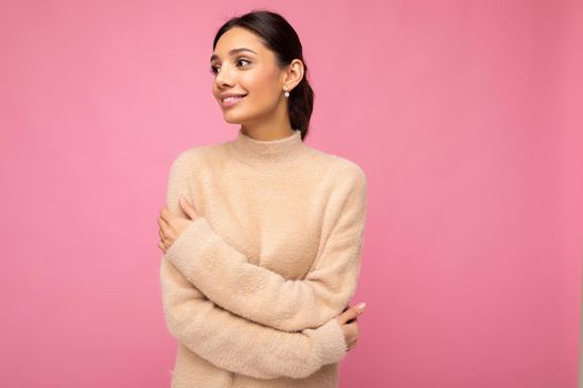 Portrait of beautiful positive cheerful cute smiling young brunette woman in casual beige sweater isolated on pink background with copy space.