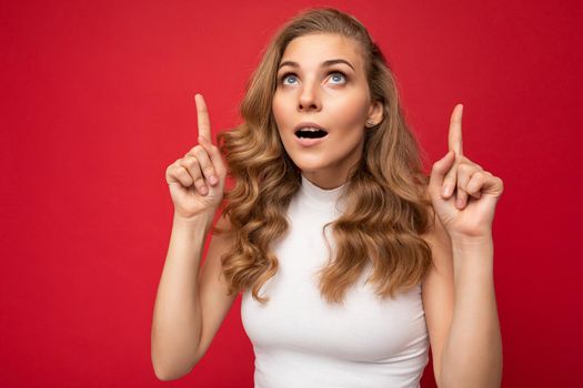 Photo of attractive positive surprised young woman pointing fingers up at copyspace presenting ads promo with wow omg sincere emotions wearing good look outfit isolated over background with free space.
