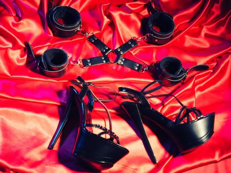 Top view of bdsm outfit. Bondage and a pair of black high-heeled shoes on the red linen. Adult sex games. Kinky lifestyle. -Image toned
