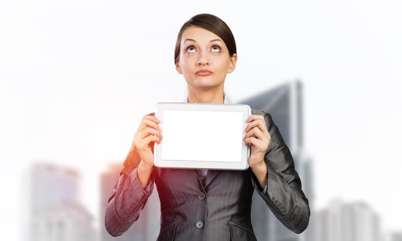 Businesswoman holding tablet computer with blank screen. Beautiful woman in business suit show tablet PC and looking upward. Corporate businessperson on downtown background. Digital technology layout