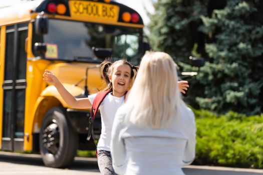 Kids student running into mother's hands to hug her after back to school near the school bus