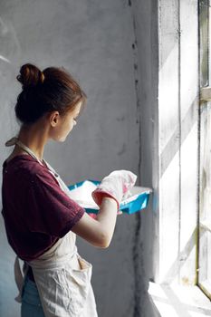 Woman in a white apron paints a window in a house interior renovation. High quality photo