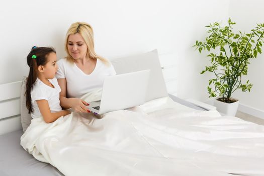 Young mother with toddler child working on the computer from home in bed