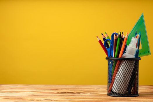 School supplies on wooden desk against yellow background front view