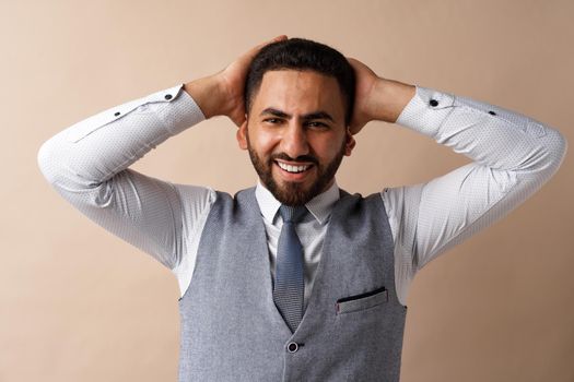 Smiling young man with hands behind head against beige background, close up