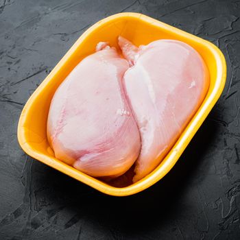 Fresh chicken breast meat in open tray, on black background