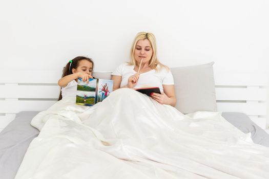 Cute little girl and her mother lying on a bed.