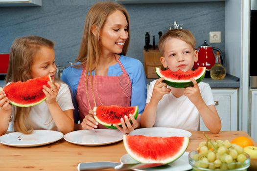Sweet family, mother and her kids eating watermelon in their kitchen having fun, close up