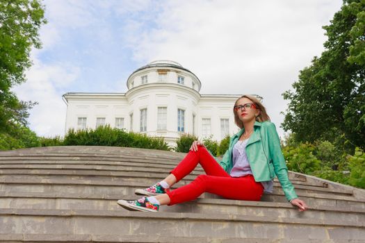 Portrait of a beautiful european woman in leather jacket and red jeans sitting om steps