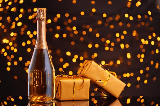 Champagne bottle and wrapped gift on blurred background of Christmas lights front view