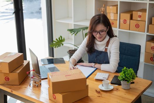 Starting Small business entrepreneur SME freelance,Portrait young woman working at home office, BOX,smartphone,laptop, online, marketing, packaging, delivery, SME, e-commerce concept