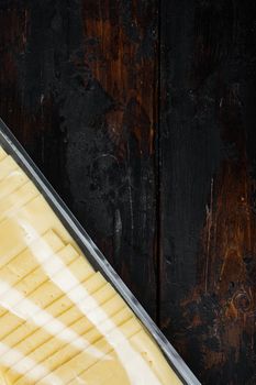 Slices of yellow cheese, sealed pack, on dark wooden background with copy space for text