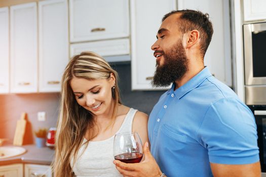 Cheerful smiling couple cooking and drinking wine in kitchen at home