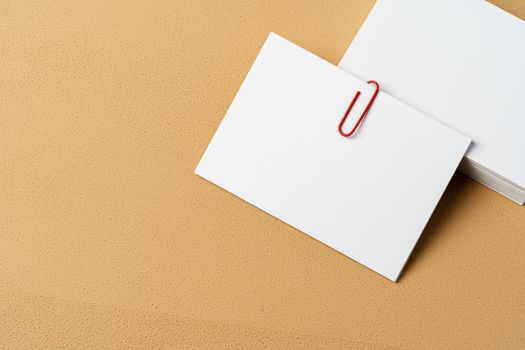 Pile of white businesscards with a clip on beige background, copy space